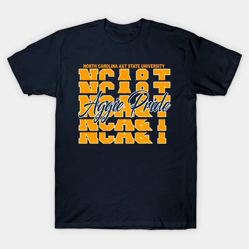 May include: A navy blue short-sleeve t-shirt featuring the text North Carolina A&T State University in orange at the top, followed by five rows of the orange text NC A&T, and the white cursive script text Aggie Pride layered across the center.