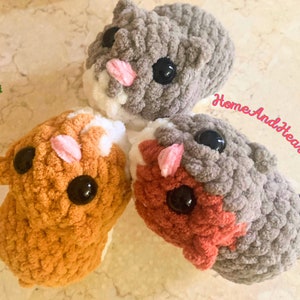 Puede incluir: Tres peluches de hámster de crochet en diferentes colores: naranja, gris y rojo. Los peluches tienen ojos negros y narices rosas.