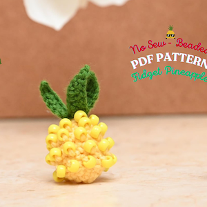May include: A yellow beaded pineapple with green crocheted leaves. The pineapple is a no-sew beaded fidget toy. The text "No Sew - Beaded PDF PATTERN Fidget Pineapple" is written in white letters on a red background.