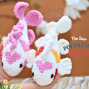 May include: Two handmade crochet koi fish in white and pink, with heart-shaped markings. One fish has pink accents, the other has orange and yellow accents. The text "No Sew PDF Pattern Heart Koi" is visible.