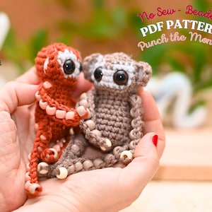 Puede incluir: Dos pequeños monos de ganchillo hechos a mano con detalles de cuentas. Uno es de color rojo anaranjado, el otro es marrón. Ambos tienen ojos negros grandes y están sostenidos en las manos de una persona. El texto "No Sew - Beaded PDF PATTERN Punch the Monkey" es visible.