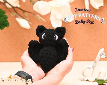 Puede incluir: Un juguete de peluche de murciélago bebé de crochet negro con ojos morados. El juguete está siendo sostenido en las manos de una persona. El texto "Low-sew PDF PATTERN Baby Bat" es visible en la imagen.