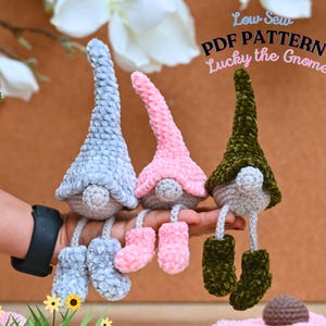 May include: Three plush gnomes in pastel colors: light blue, pink, and olive green. Each gnome has a long, pointed hat, a round nose, and dangling legs with matching boots. The text "Low Sew PDF Pattern Lucky the Gnome" is visible.