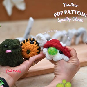 Op de afbeelding: Drie handgemaakte gehaakte stressballen in de vorm van spookachtige karakters. Eén is donkergroen met een roze mond, een andere is oranje en zwart, en de derde is wit met een rode hoed en een groen centrum. De tekst "No Sew PDF PATTERN Spooky Ghost" is zichtbaar.