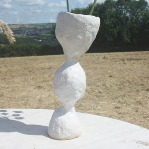 Pode incluir: Vaso de cerâmica branca com uma superfície texturizada e uma forma orgânica única. O vaso é alto e fino, com uma abertura larga na parte superior e uma base estreita.