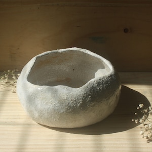 May include: White ceramic bowl with a textured, uneven surface. The bowl has a rounded shape and a wide, shallow opening.