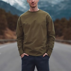 Puede incluir: Una camisa de manga larga de color verde oliva con cuello redondo.