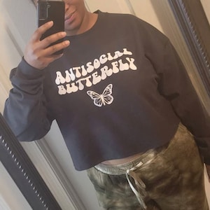 May include: A black cropped sweatshirt with the text "ANTISOCIAL BUTTERFLY" in white, stylized lettering. A white butterfly graphic is centered below the text.