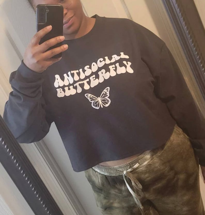 May include: A black cropped sweatshirt with the text "ANTISOCIAL BUTTERFLY" in white, stylized lettering. A white butterfly graphic is centered below the text.