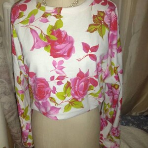 May include: White long-sleeved cropped top with a pink and green floral print.