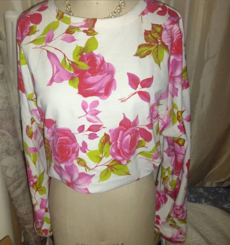 May include: White long-sleeved cropped top with a pink and green floral print.