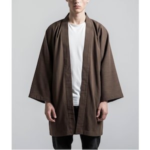May include: A brown kimono-style jacket with wide sleeves. The open-front jacket is worn over a white t-shirt. The jacket is made of a textured fabric and has a relaxed fit. The model is wearing black pants.