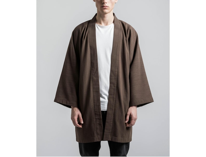 May include: A brown kimono-style jacket with wide sleeves. The open-front jacket is worn over a white t-shirt. The jacket is made of a textured fabric and has a relaxed fit. The model is wearing black pants.