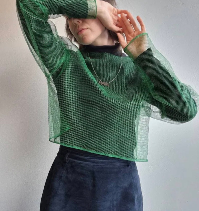May include: A green mesh long-sleeved shirt with a high neckline. The shirt is made of a sparkly material and has a loose fit.