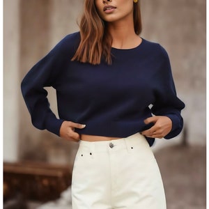 May include: A navy blue long-sleeved sweater with a round neckline. The sweater is cropped and has a relaxed fit.
