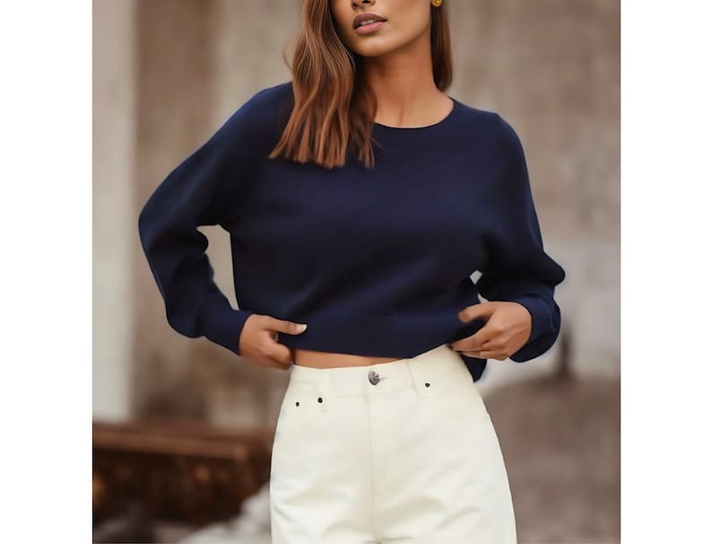 May include: A navy blue long-sleeved sweater with a round neckline. The sweater is cropped and has a relaxed fit.