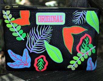 May include: Black leather clutch with a zipper closure and a colorful tropical leaf design. The clutch has a patch that says "ORIGINAL" in pink and white letters.