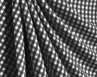 May include: Black and white gingham fabric with a checkered pattern. The fabric is folded and draped, showing the texture and weave.
