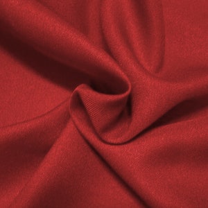 May include: Close-up of a deep red fabric with a smooth, textured surface. The fabric is folded and draped, creating soft folds and curves.
