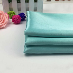 May include: Stack of four light blue satin fabric swatches. The fabric is smooth and silky.