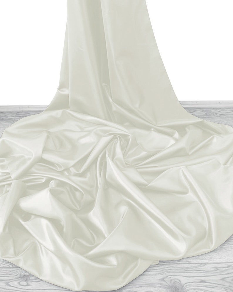 May include: A white satin fabric draped over a wooden surface. The fabric is smooth and silky, with soft folds and wrinkles.