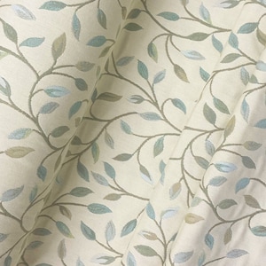 May include: A cream-coloured fabric with a repeating pattern of green and blue leaves on brown vines.
