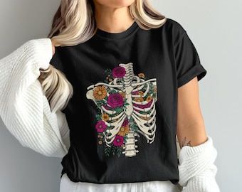 May include: Black t-shirt featuring a detailed illustration of a human rib cage filled with colorful flowers. The design includes yellow sunflowers, pink roses, and green foliage, creating a unique and artistic floral skeleton design.