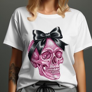 May include: White t-shirt featuring a pink glitter skull with a black bow. The skull design has detailed facial features and is centered on the shirt. The shirt is a casual style, suitable for everyday wear.