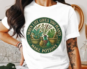 Könnte beinhalten: Weißes T-Shirt mit einem kreisförmigen Aufdruck mit dem Text "WHEN LIFE GIVES YOU PLANTS MAKE POTIONS". Das Design umfasst Illustrationen von Pflanzen, Mörsern und Stößeln sowie Flaschen mit grünen, braunen und goldenen Tränken.