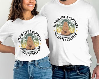 Puede incluir: Dos camisetas blancas con un gráfico de un capibara sentado en una pose relajada con el texto "Sitting like a capybara perfectly relaxed".