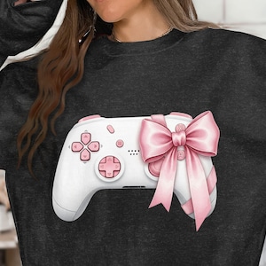 Op de afbeelding: Witte gamecontroller met roze knoppen en een grote roze strik. De controller heeft een klassiek ontwerp met een navigatiepad en actieknoppen. De strik voegt een decoratief tintje toe aan het gaming-accessoire.
