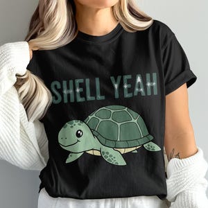 Könnte beinhalten: Schwarzes T-Shirt mit einer Schildkröten-Cartoon-Grafik. Die Schildkröte ist grün mit einem gemusterten Panzer und einem lächelnden Gesicht. Der Text "SHELL YEAH" steht in grünen Buchstaben über der Schildkröte.