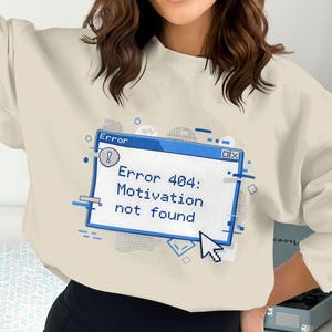 Peut inclure: Sweat-shirt beige avec un motif bleu et blanc représentant un message d'erreur informatique. Le message indique "Error 404: Motivation not found" avec un curseur pixélisé. Le sweat-shirt a des manches longues et un col rond.