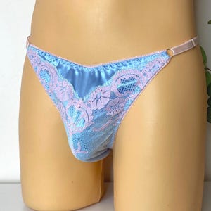 Può includere: Perizoma in raso azzurro con dettagli in pizzo lavanda. La delicata lingerie presenta un design a vita bassa con una sottile fascia in vita e un motivo floreale in pizzo lungo i bordi. Il tessuto ha una leggera lucentezza.