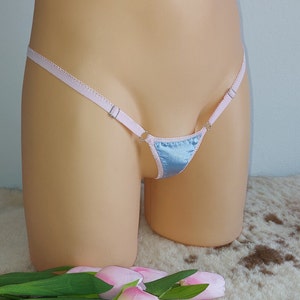 May include: A light blue satin thong with pink trim and adjustable straps. The thong is on a mannequin.