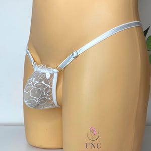 May include: White floral lace thong underwear with a thin, adjustable waistband. The underwear features a delicate floral pattern and a minimalist design. The garment is displayed on a mannequin.