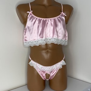 May include: A pink satin lingerie set with white lace trim. The top has a ruffled neckline and adjustable straps. The bottom is a thong style with a cutout in the back.