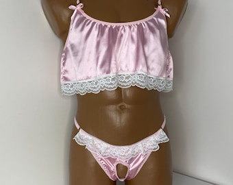May include: A pink satin lingerie set with white lace trim. The top has a ruffled neckline and adjustable straps. The bottom is a thong style with a cutout at the back.