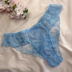 Può includere: Un perizoma azzurro realizzato in tessuto a rete trasparente con un intricato bordo in pizzo floreale. Il capo è caratterizzato da una delicata fascia in vita e pannelli laterali in pizzo smerlato, con un design semi-trasparente su tutta la superficie.