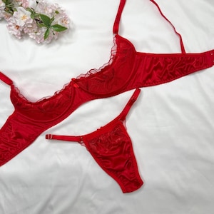 Può includere: Un set di lingerie rosso vivace composto da un reggiseno e un perizoma. Il reggiseno presenta coppe con ferretto con delicati ricami floreali, pannelli in rete trasparente e spalline regolabili. Il perizoma abbinato ha una finitura satinata.