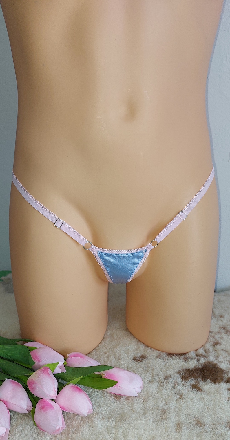 May include: A light blue satin triangle-shaped lingerie with pink satin straps and silver metal rings.