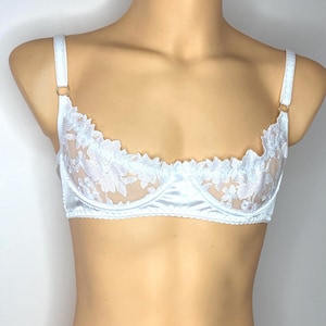 Könnte beinhalten: Ein hellblauer BH mit floralen Spitzendetails. Der BH hat einen Unterbrustbereich und Träger aus Satin mit zarten Spitzencups. Die Träger sind verstellbar und werden mit goldfarbenen Ringen an den Cups befestigt. Der BH wird auf einer Schaufensterpuppe präsentiert.