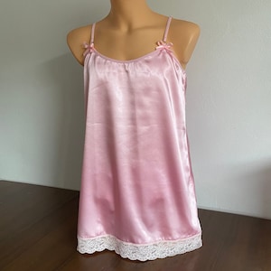 Könnte beinhalten: Ein rosafarbenes Satin-Schlafkleid mit verstellbaren Trägern und einem Spitzenbesatz. Das Kleid hat ein schlichtes, elegantes Design.
