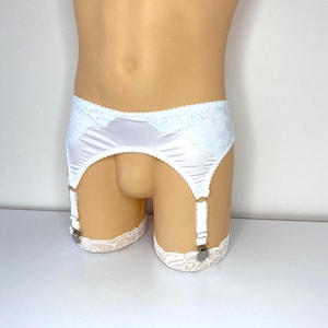 Könnte beinhalten: Weißer Satin-Strumpfhalter mit Spitzenbesatz. Der Strumpfhalter hat vier verstellbare Träger mit Metallverschlüssen. Der Bund ist mit Spitze verziert. Das Kleidungsstück wird auf einer Schaufensterpuppe präsentiert.