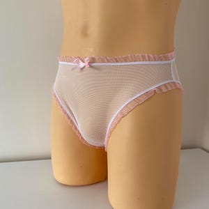 May include: Sheer, light pink underwear with white trim and ruffled edges. A small pink bow adorns the front. The delicate lingerie is designed with a mesh fabric.