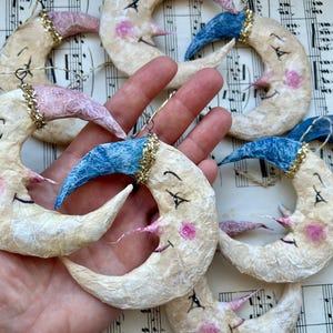 Adorno de luna creciente con cara y gorro de dormir elaborado en cartón reciclado y papel maché con purpurina de cristal en azul y rosa