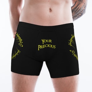 May include: Black boxer shorts with a yellow inscription that reads "YOUR PRECIOUS" and a yellow design of an inscription in a circle around the inscription.