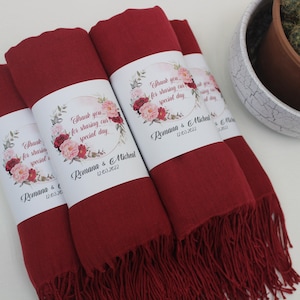 May include: Four burgundy red pashmina scarves with floral and gold accents. Each scarf has a white label with the text "Thank you for sharing our special day" and the names "Romana & Michael" and the date "12.03.2022".