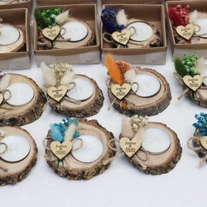 May include: A collection of rustic wooden candle holders, each with a white candle, decorated with dried flowers and a wooden heart with the names "Jordan & Alexis" engraved. Some are in small cardboard boxes.