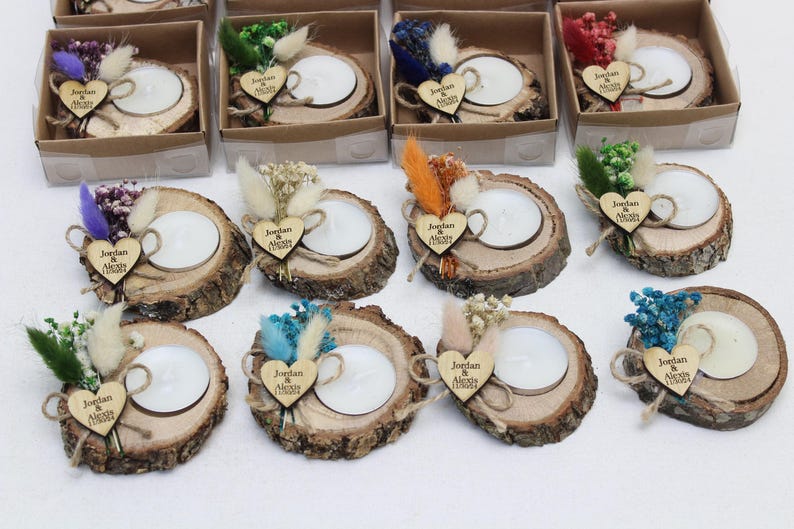 May include: A collection of rustic wooden candle holders, each with a white candle, decorated with dried flowers and a wooden heart with the names "Jordan & Alexis" engraved. Some are in small cardboard boxes.